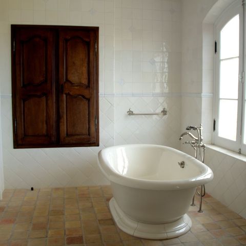 Freestanding soaking tub beside an arched window and a carved wood cabinet
