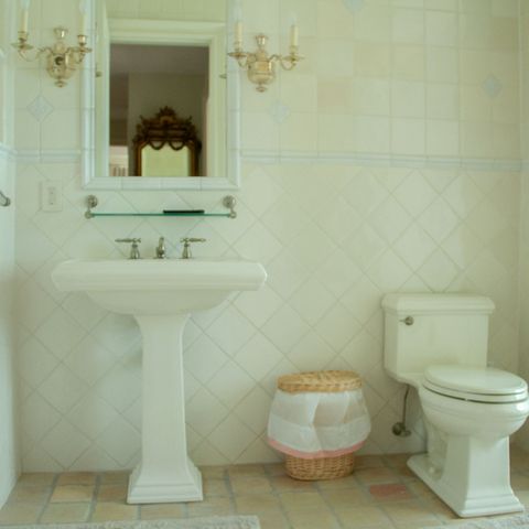 Pedestal sink and toilet under a gilt mirror with wall sconces