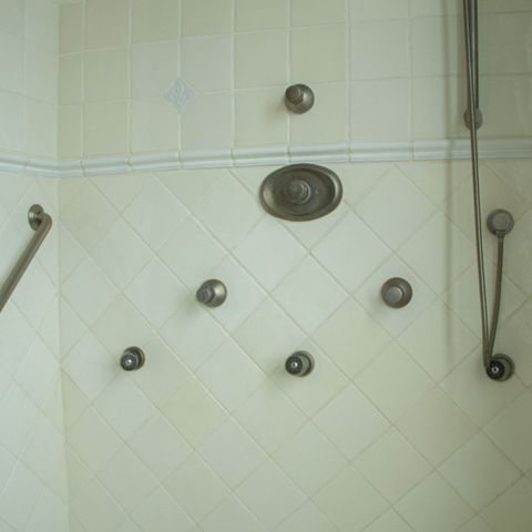 Shower wall with body sprays, a hand shower and a grab bar on diagonal tile