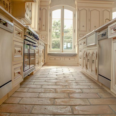 Long galley kitchen with cream cabinetry, a terracotta tile floor and an arched window