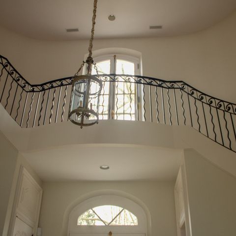 Sweeping staircase with a wrought-iron balcony rail and a pendant light