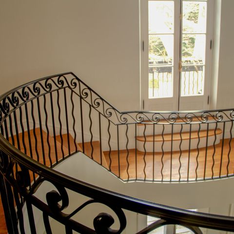 Curved staircase with a wrought-iron railing overlooking a sunlit landing